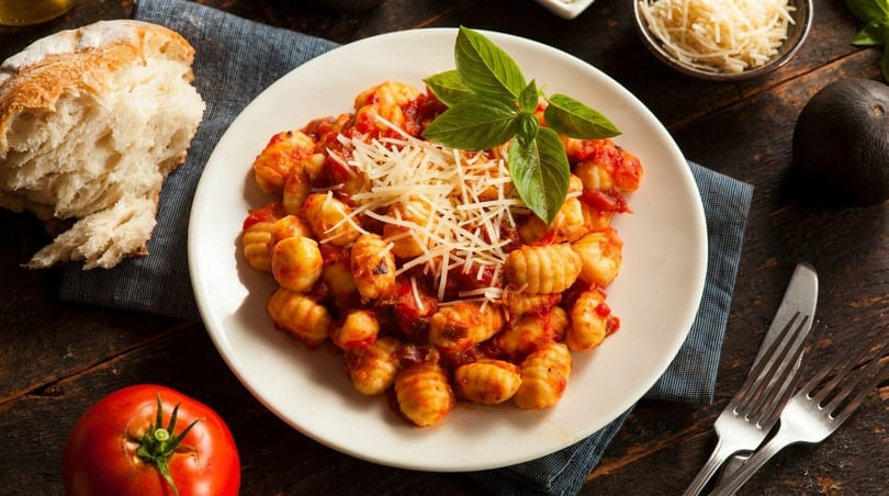 Plate of gnocchi with tomato sauce, parmesan, and basil, next to bread, tomato, and avocado.